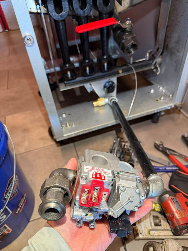 Holding the new gas valve after installation, with the fryer's burner assembly and manifold visible in the background.
