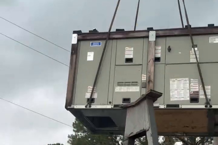 A close look at a rooftop unit in the air: rigging, balance, and clearances are checked before the lift.