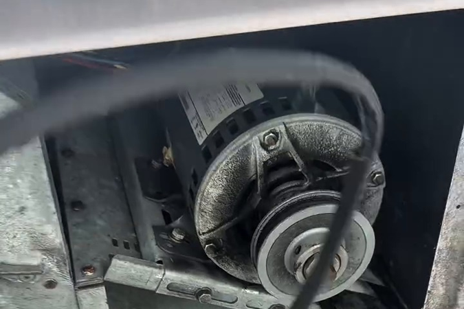 The blower motor and belt assembly inside the rooftop cabinet.